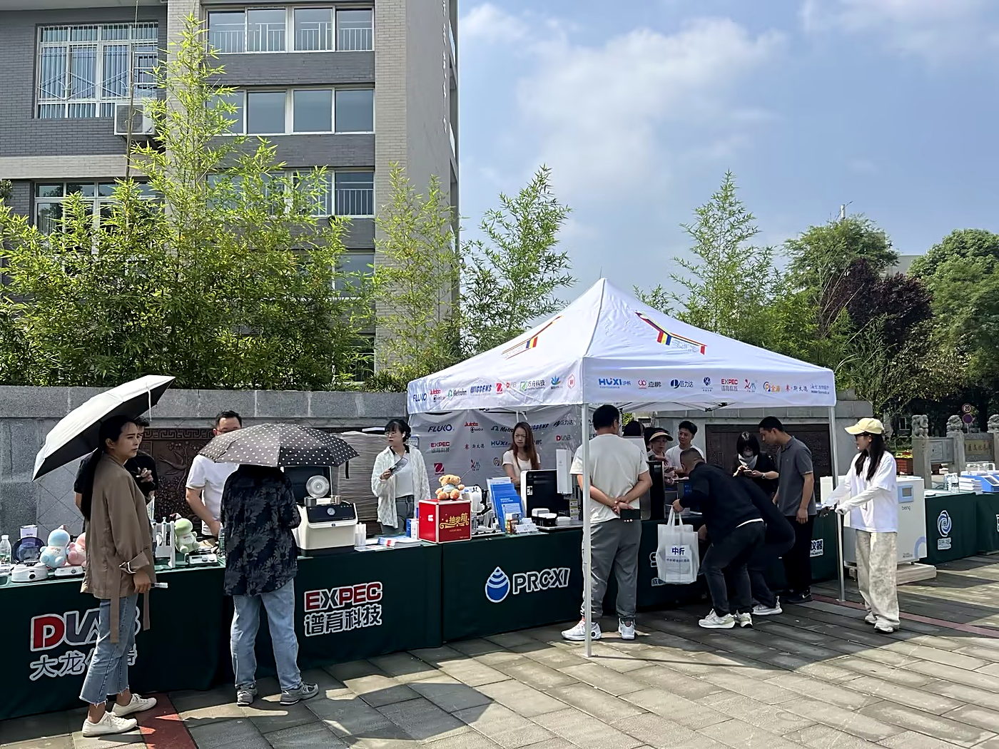 联合摆展现场,绿色桌布前数十家品牌陈列产品,观众在展位前咨询