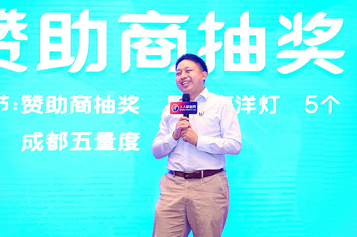 活动舞台现场,主持人手持话筒,背景板写有赞助商抽奖与成都五量度